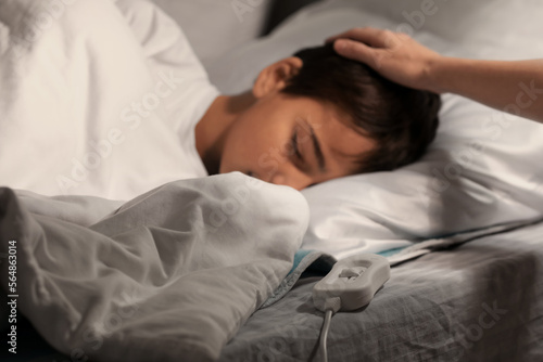 Woman and her little boy sleeping on electric heating pad in bedroom at night