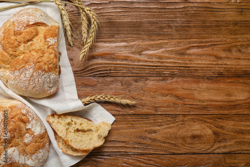Napkin with loaves of fresh bread and wheat ears on wooden background