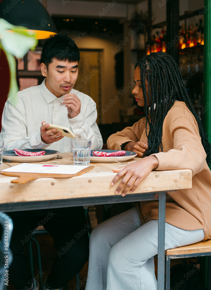 Couple looking at mobile sitting in restaurant table Couple looking at mobile sitting in restaurant table