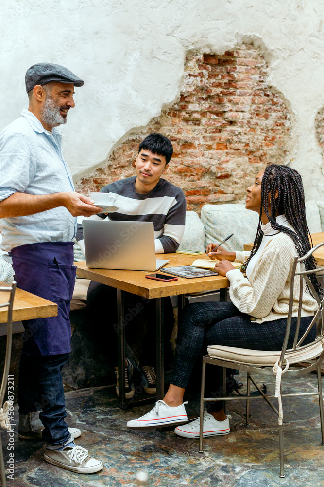 friendly Cafe waiter talking to young customers in business meeting friendly Cafe waiter talking to young customers in business meeting