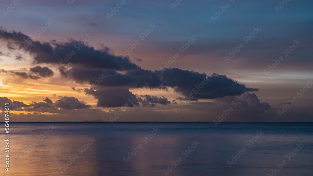Beautiful tropical sunset. Purple clouds float in the sky, illuminated with pink and gold. Reflection on the surface of a calm ocean. Long exposure. Seychelles
