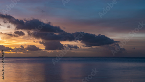 Beautiful tropical sunset. Purple clouds float in the sky, illuminated with pink and gold. Reflection on the surface of a calm ocean. Long exposure. Seychelles