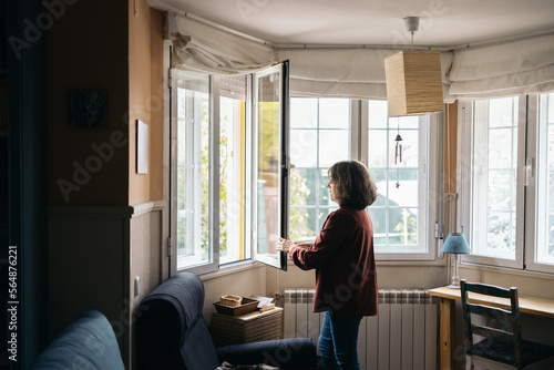 Middle-aged woman opening the window at home