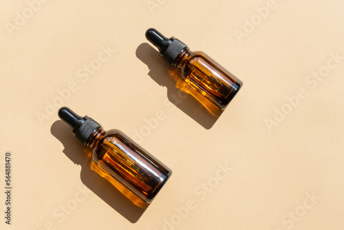 Top view of amber glass vials with cosmetic serum. Containers without labeling for cosmetics with dropper lids on beige background with hard shadow. Flatley, copyspace