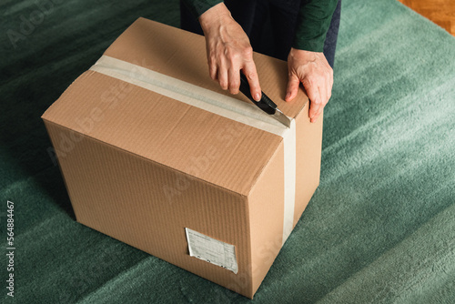 Middle-aged adult woman opening clothing delivery box using cutter photo