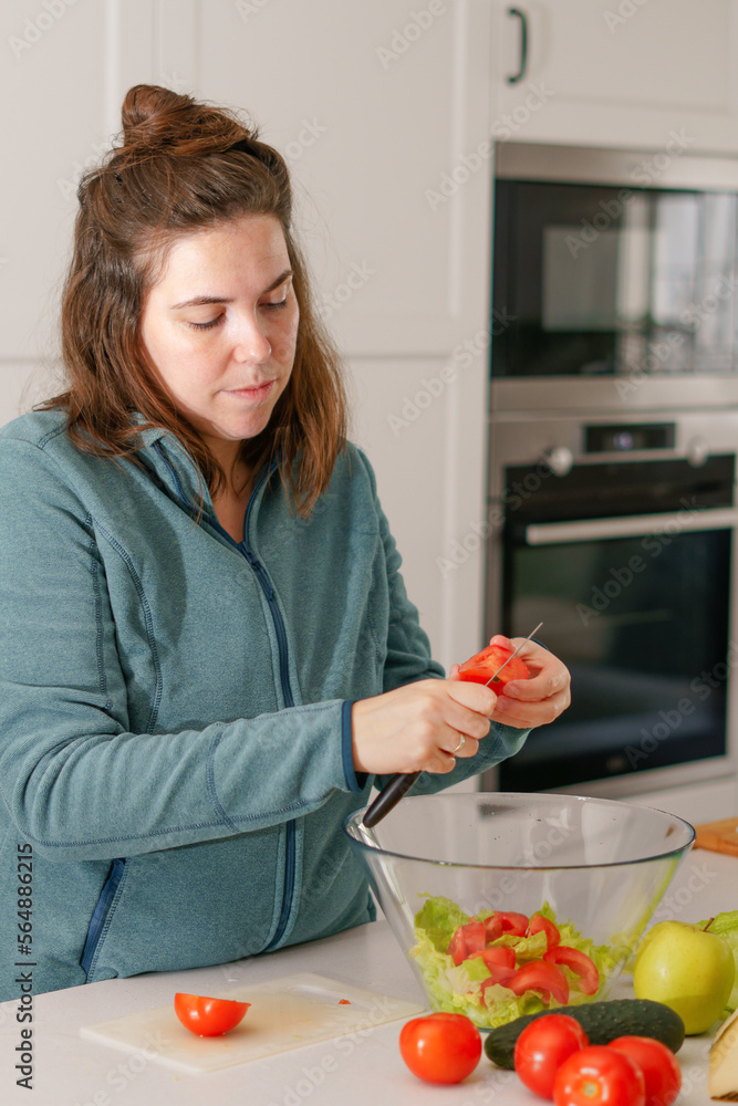 long-haired brunette girl cutting tomatoes to prepare a salad in her home kitchen