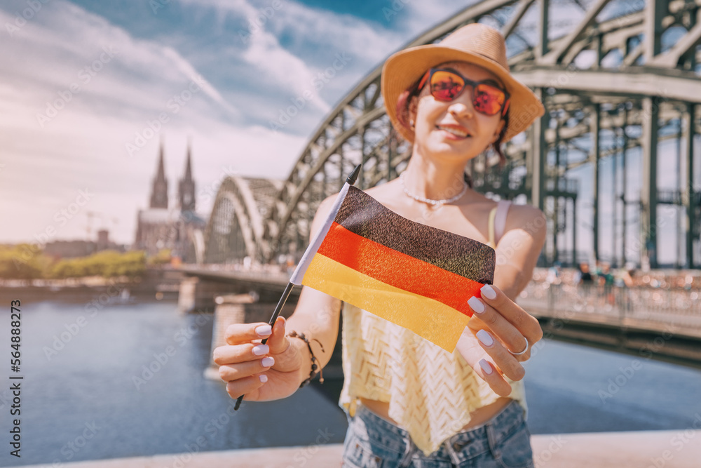 Happy girl holding a German flag against the Rhine bridge and Cologne Dom Cathedral. Travel landmarks and traditional holidays
