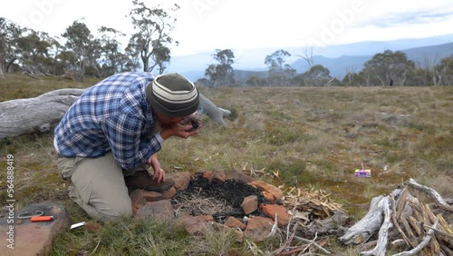 A man blows on a tinder buddle to get a fire going in the Australian mountains. photo