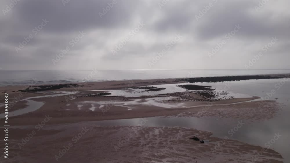Smooth aerial shot of a wet beach in Cacela Velha, Portugal, with still water with an overcast sky