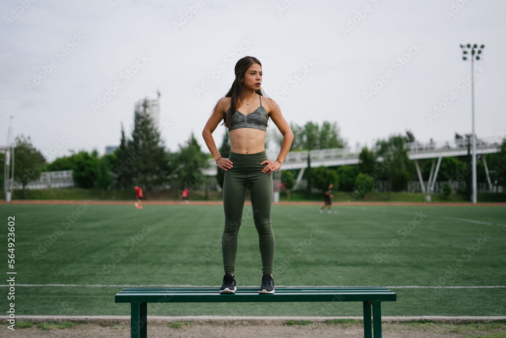 © Bianca Beltran/Stocksy - Sporty Latina woman standing on a bench in a confident posture.