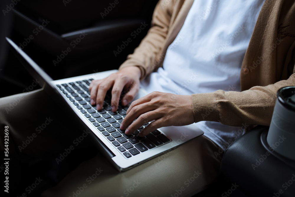 Asian man sitting on back car seat, typing on laptop Asian man sitting on back car seat, typing on laptop