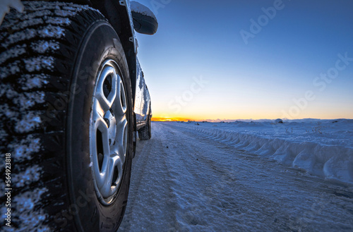 Perspective wheel of 4x4 car with ice on a completely snowy road with tire tracks that goes to the horizon with a golden and magical Icelandic sunrise. The light of dawn is reflected in the car.
