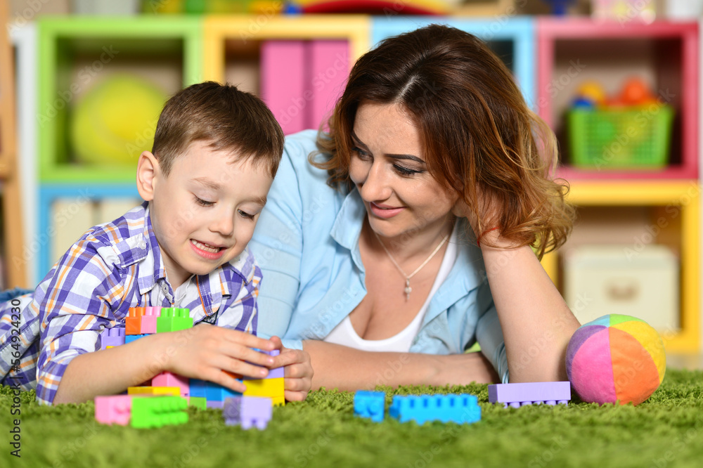 Fototapeta premium Woman and son playing with plastic blocks on floor