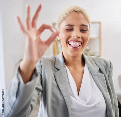 Portrait, tongue and emoji with a business black woman winking in her office at work to gesture a perfect hand sign. Face, motivation and succes with a female employee feeling happy or proud photo