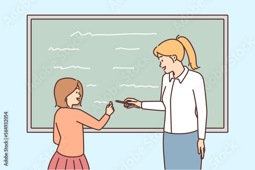 Female teacher and schoolgirl writing on blackboard 