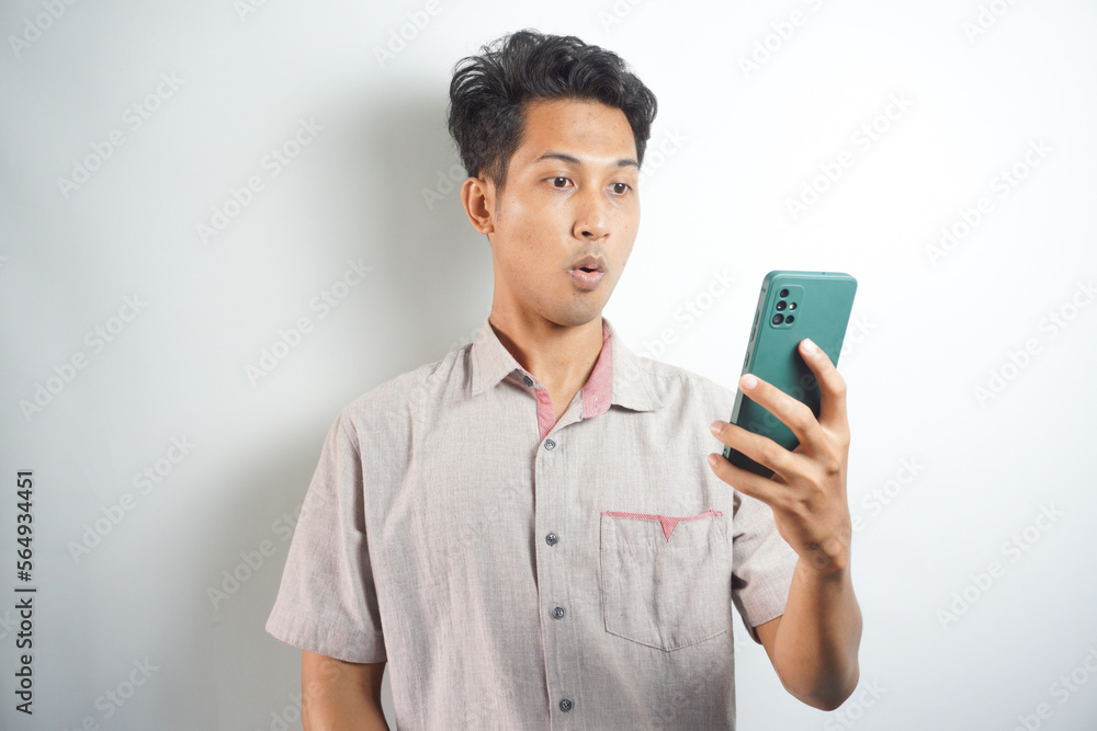 Amazed shocked asian guy holding smartphone in his hand, looking at the phone in surprise, stunned facial expression, stands on isolated white background Amazed shocked asian guy holding smartphone in his hand, looking at the phone in surprise, stunned facial expression, stands on isolated white background