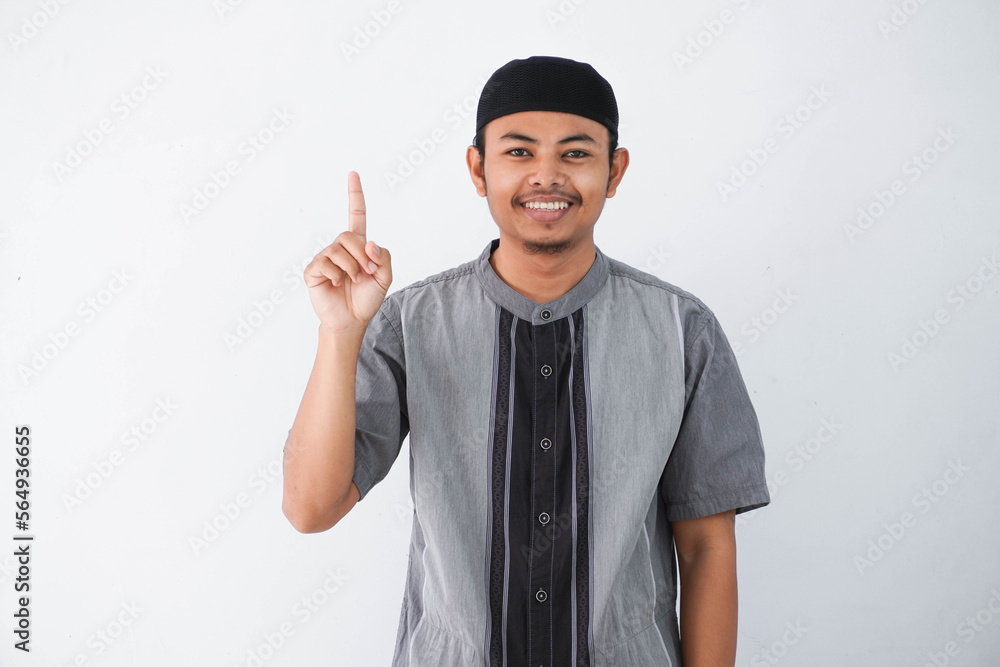 young asian muslim man finger pointing up raising a finger got a good idea looks surprised with a smile wearing grey koko clothes, isolated on a white background. young asian muslim man finger pointing up raising a finger got a good idea looks surprised with a smile wearing grey koko clothes, isolated on a white background.