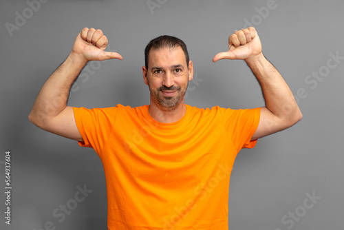 Photo of happy latino man with beard charming good mood smile pointing finger to himself isolated over gray color background.