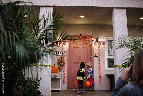 Rear view of siblings wearing costumes while trick or treating on porch during Halloween