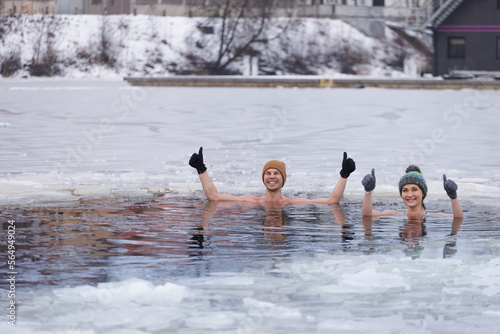 Winter swimming. Young couple ready to swim in ice water. Tea after plunge in cold water. Man and woman wrapped in a towel and swimming clothes. Hat and gloves. People and nature lake in the city