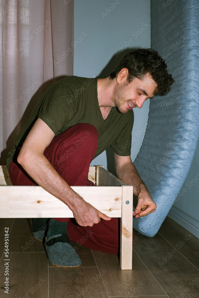 Smiling man assembles a wooden bed Smiling man assembles a wooden bed