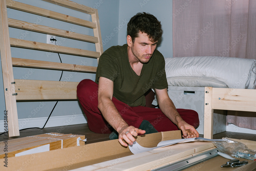 A curly-haired man studies the instructions for assembling a new bed A curly-haired man studies the instructions for assembling a new bed