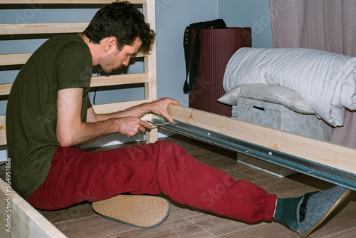 A young man enthusiastically assembles a wooden bed 