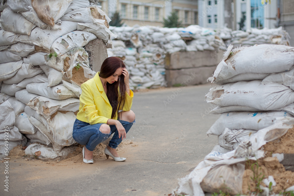 A woman, a Ukrainian patriot, sit on the street of the city at the war in Ukraine, among the barricades of sandbags. She is dressed in the colors of the Ukrainian flag.
