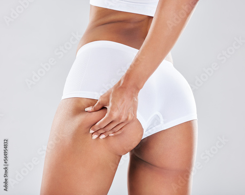 Cellulite, stretch marks and woman touching her butt for insecurity isolated on grey studio background. Sexy, liposuction and hand of a girl feeling her body for fat, health and treatment on backdrop