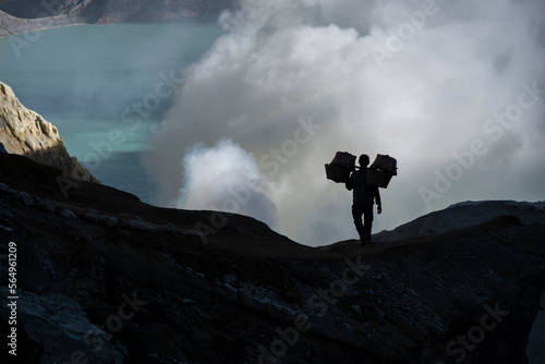 Silhouette of sulfur miner carrying heavy load of Sulphur at top of Kawah Ijen Volcano, Java, Indonesia photo