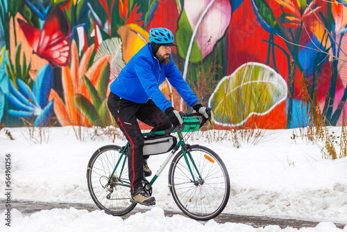 A bearded man rides a bicycle in a winter park against the background of a multi-colored wall. Eco-friendly transport in winter. Active lifestyle