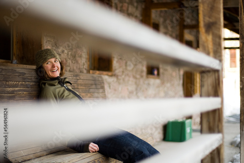 Female relaxing on a bench outside a rustic building. Smiling face and laid back look.