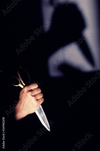 Hand and silhouette of a hand holding scissors as a weapon.