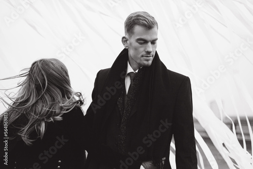 Beautiful stylish and fashionable couple in a suit, dress and coat with gloves on a classic photo shoot in a photo studio and on the street, where they look at each other, hold hands and hug.