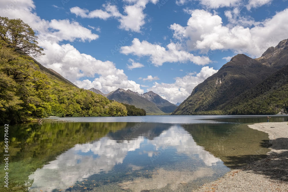 A man fishing from the banks of the calm waters of Lake Gunn in the South Island of New Zealand with David Peaks in the distance