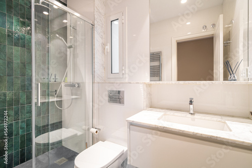 This bathroom boasts a fresh and modern look with its combination of green and white tiles  sleek shower  spacious sink  large mirror  and a radiator reflected in it.
