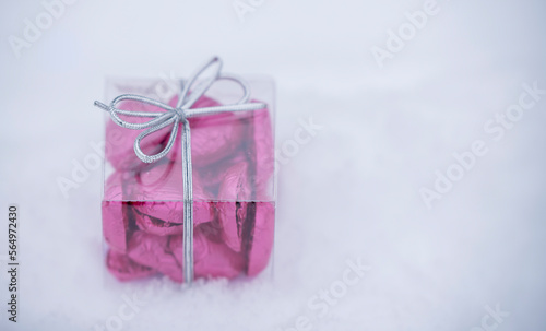 a small transparent box with heart-shaped chocolates inside, lying on the snow