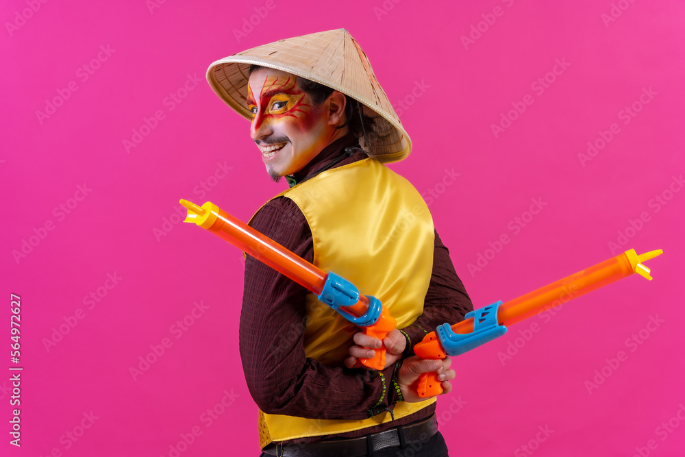 Portrait of a clown with white facial makeup on a pink background, with toy guns and a Chinese hat Portrait of a clown with white facial makeup on a pink background, with toy guns and a Chinese hat