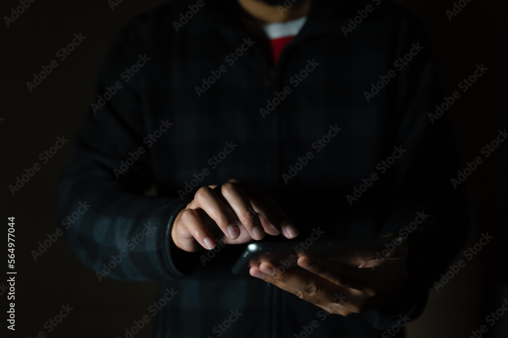 Cheerful bearded man in black long sleeve shirt using digital tablet in Dark room. hand holding tablet. 