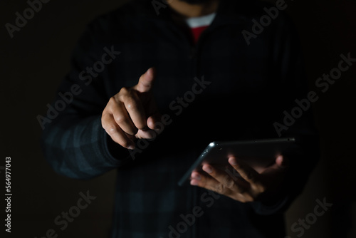 Cheerful bearded man in black long sleeve shirt using digital tablet in Dark room. hand holding tablet.  © arneaw