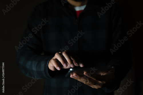 Cheerful bearded man in black long sleeve shirt using digital tablet in Dark room. hand holding tablet.  © arneaw
