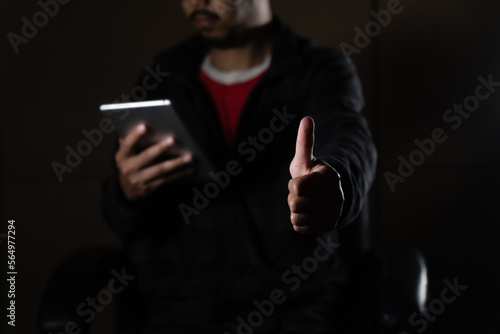 Cheerful bearded man in black long sleeve shirt using digital tablet in Dark room. hand holding tablet.  © arneaw