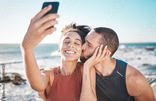 Selfie kiss, gratitude and couple with a phone for streaming, training and love at the beach in Bali. Caring, exercise and affectionate man and woman with a smile for a mobile photo after a workout