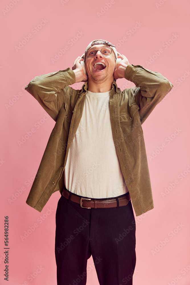 Burst of laugh. Young positive man posing, emotionally listening to music in headphones over pink studio background. Concept of emotions, facial expression, lifestyle, retro fashion. Ad Burst of laugh. Young positive man posing, emotionally listening to music in headphones over pink studio background. Concept of emotions, facial expression, lifestyle, retro fashion. Ad