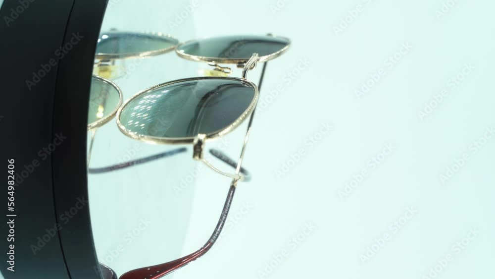 A vertical close up cinematic shot of laying golden sunglasses on a 360 rotating stand, reflecting lights on the tanned glass, studio light, product 4K video, slow motion. A vertical close up cinematic shot of laying golden sunglasses on a 360 rotating stand, reflecting lights on the tanned glass, studio light, product 4K video, slow motion.