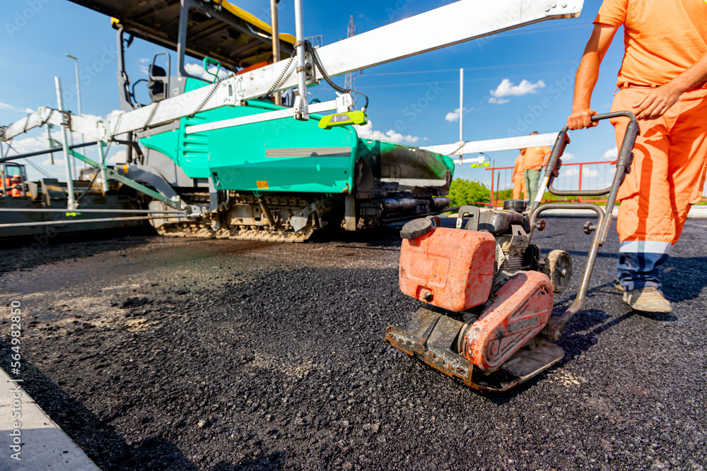 Worker compacts tarmac using vibration plate compactor