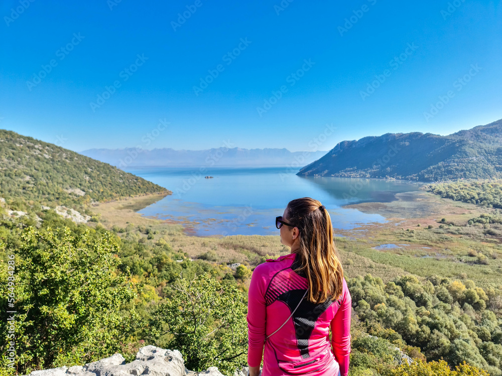 Naklejka premium Rear view of woman with panoramic view of Lake Skadar National Park in autumn seen from Virpazar, Bar, Montenegro, Balkans, Europe. Stunning travel destination in Dinaric Alps near Albanian border