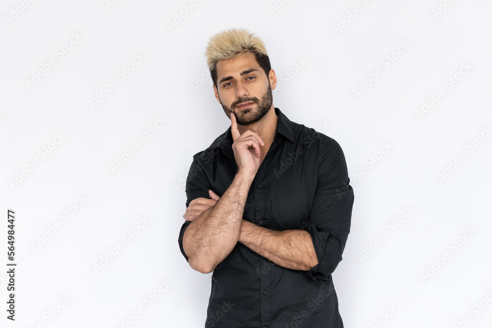 Portrait of thoughtful young man looking at camera touching chin. Caucasian guy with stubble and highlighted hair wearing black T-shirt thinking or planning. Idea concept Portrait of thoughtful young man looking at camera touching chin. Caucasian guy with stubble and highlighted hair wearing black T-shirt thinking or planning. Idea concept