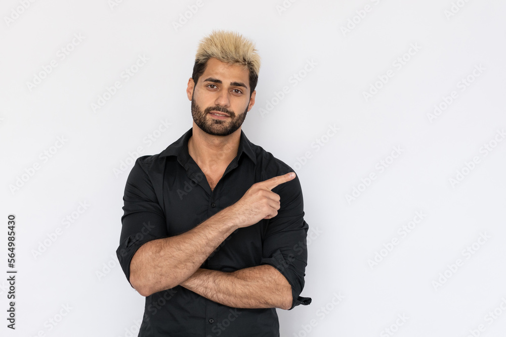 Portrait of positive young man showing direction over white background. Caucasian guy with stubble and highlighted hair wearing black T-shirt pointing finger aside and smiling. Advertising concept Portrait of positive young man showing direction over white background. Caucasian guy with stubble and highlighted hair wearing black T-shirt pointing finger aside and smiling. Advertising concept