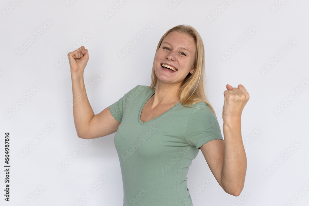 Cheerful young woman with clenched fists. Portrait of happy Caucasian female model with fair hair in green T-shirt looking at camera, smiling and celebrating success. Victory, advertising concept Cheerful young woman with clenched fists. Portrait of happy Caucasian female model with fair hair in green T-shirt looking at camera, smiling and celebrating success. Victory, advertising concept